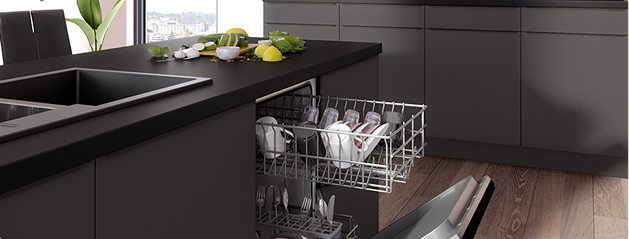 Cuisine moderne avec îlot central noir, évier intégré, lave-vaisselle ouvert rempli de vaisselle blanche, et plan de travail décoré de fruits et herbes.