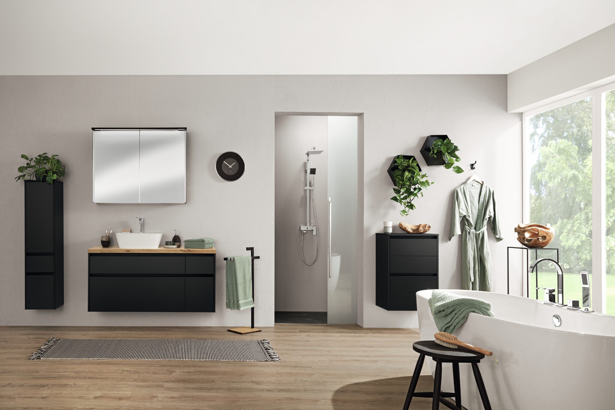 Salle de bain moderne avec meubles noirs, baignoire blanche, plantes suspendues et accessoires verts sur sol en bois clair.