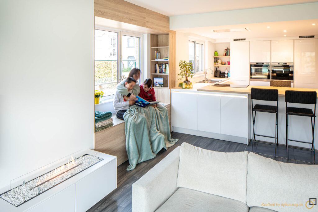 Femme avec deux enfants assis devant une fenêtre avec en arrière plan une cuisine aux façades blanches et laquées