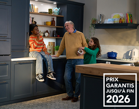 Un homme et deux enfants discutent dans une cuisine moderne avec des armoires bleues et des étagères décorées. Texte "Prix garantis jusqu'à fin 2026".