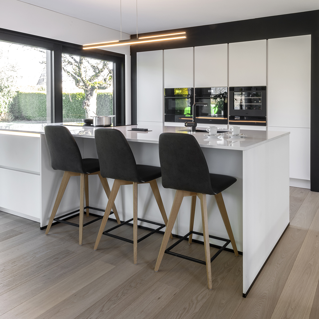 Cuisine blanche avec îlot central et plan de travail blanc. Colonnes avec électroménagers encastrés.