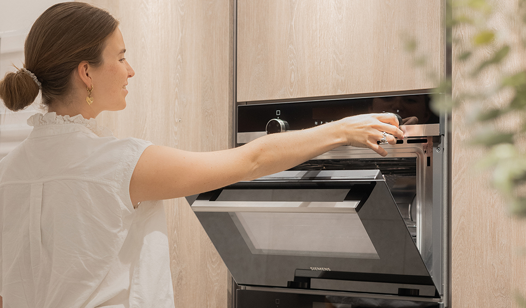 Une personne en chemise blanche ajuste le cadran d'un four encastré dans un meuble en bois clair.