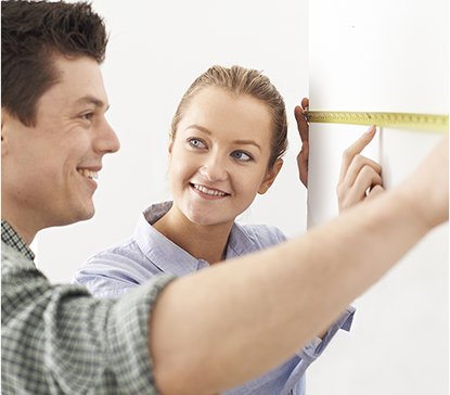 Deux personnes mesurent un mur blanc avec un ruban à mesurer jaune. L'une d'elles tient l'extrémité du ruban.