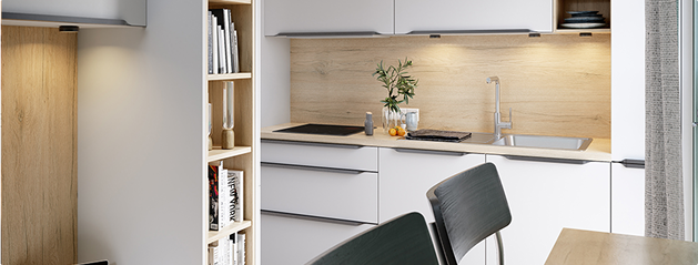 Cuisine moderne avec des armoires blanches, un plan de travail en bois clair, évier métallique, étagères de livres et chaises noires.